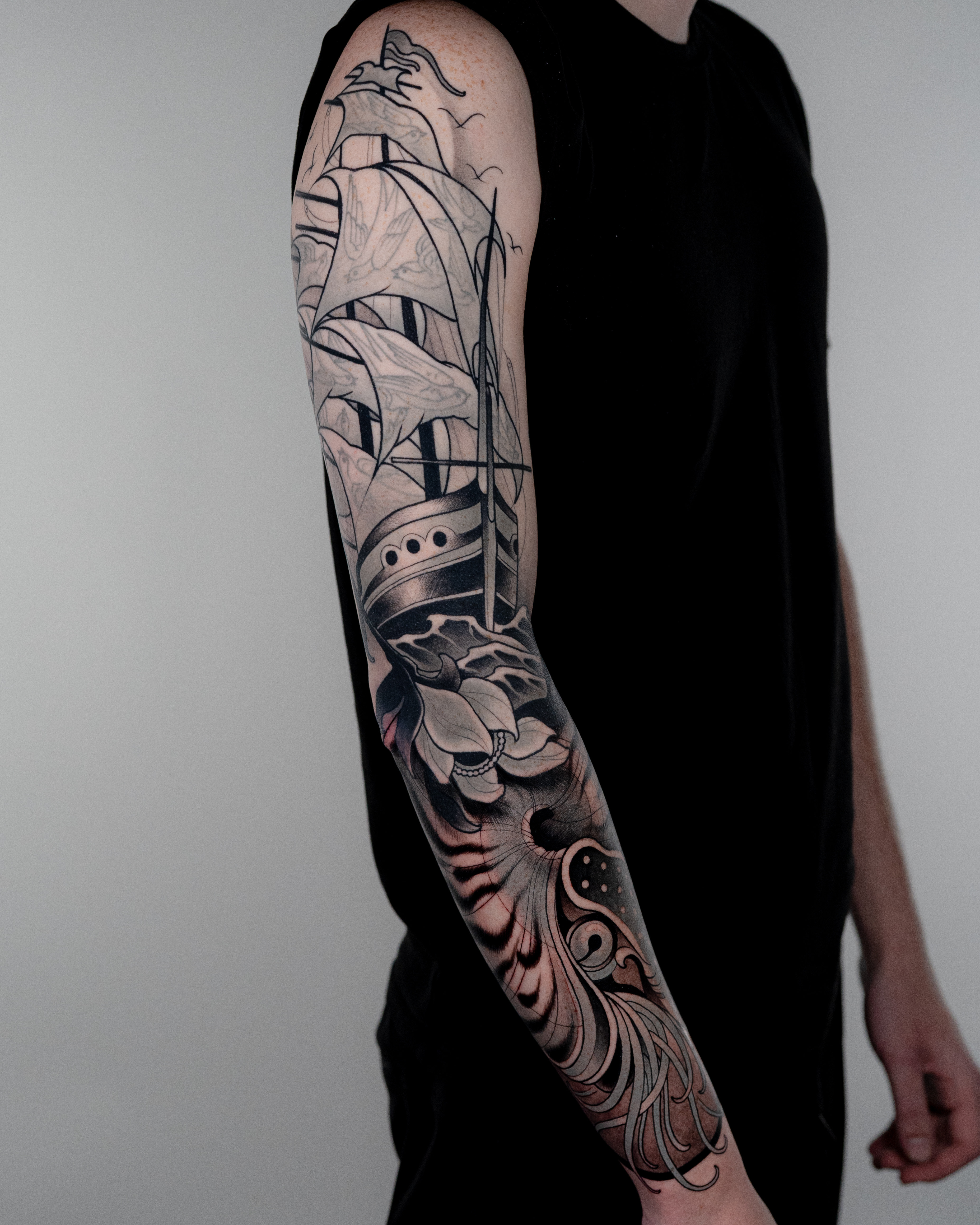 Healed black-and-grey full sleeve by Gian Karle, neo-traditional sailing ship with opaque greys, line weight hierarchy, and strong black anchors