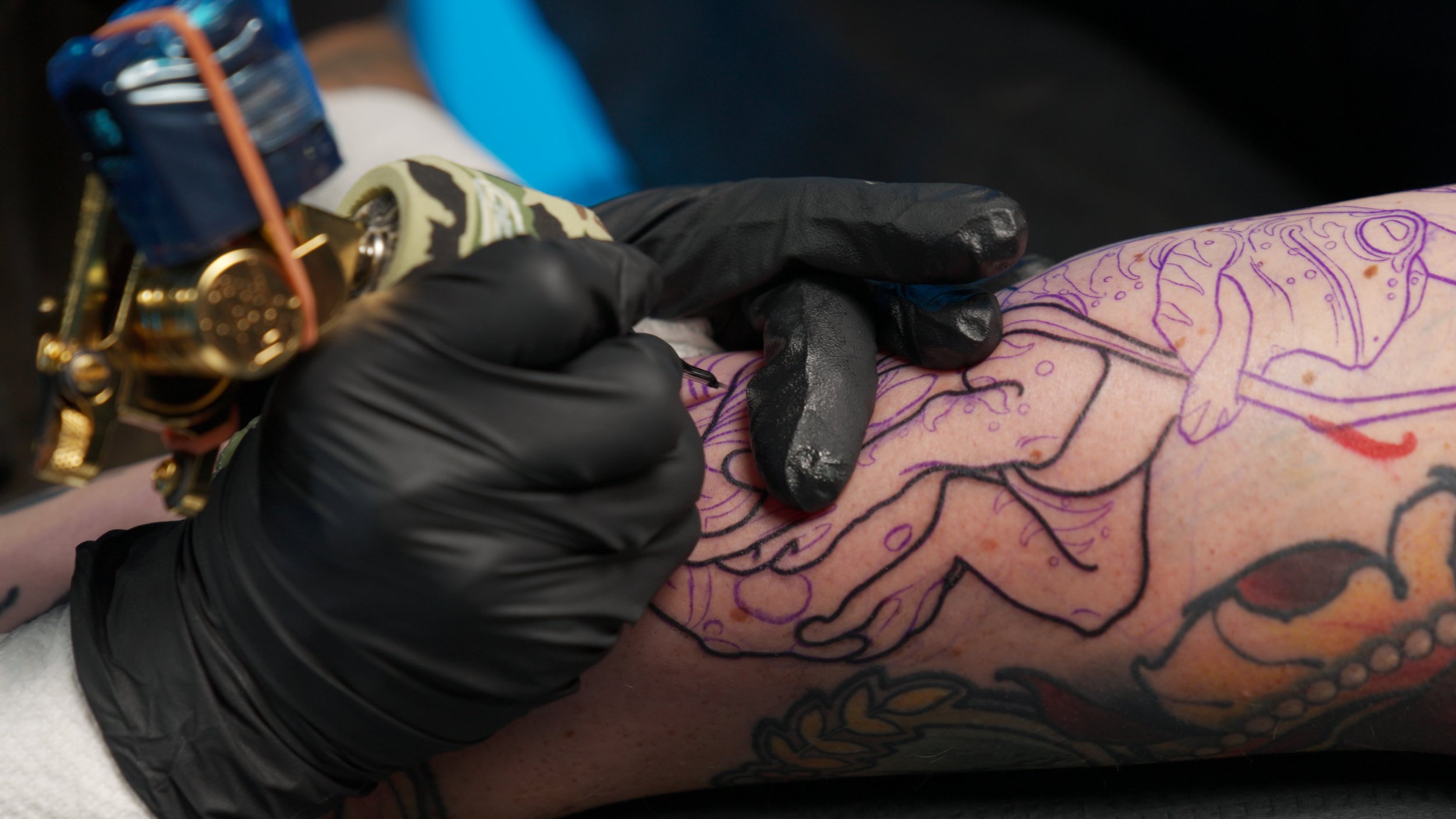 Gian pulling a bold black outline over a purple stencil on a neo-traditional sea-creature piece, line weight commitment in real time