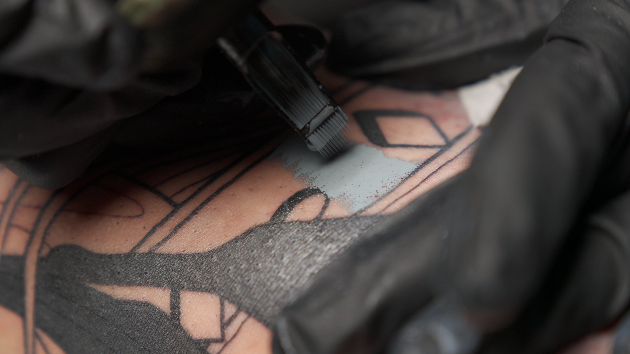 Needle packing opaque grey on linework, the technique that gives black-and-grey neo-traditional its weight